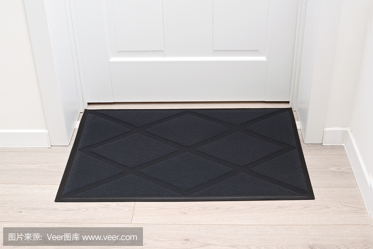 白色门前木质地板上的黑色羊毛门垫